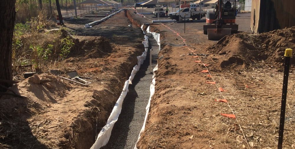 A Trench is Being Dug in the Dirt Next to a Road — Diggamen Civil Contracting in Tivendale, NT