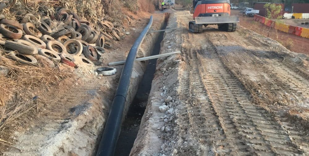 A Bulldozer is Driving Down a Dirt Road Next to a Pile of Tires — Diggamen Civil Contracting in Tivendale, NT