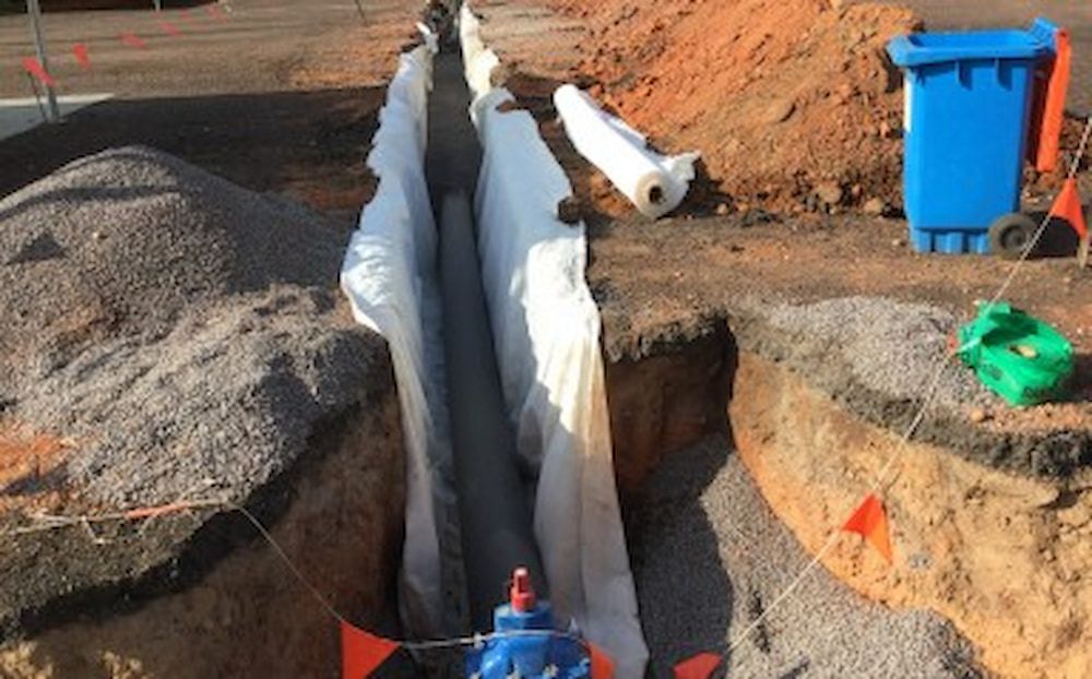A Trench is Being Dug in the Dirt Next to a Trash Bin — Diggamen Civil Contracting in Tivendale, NT