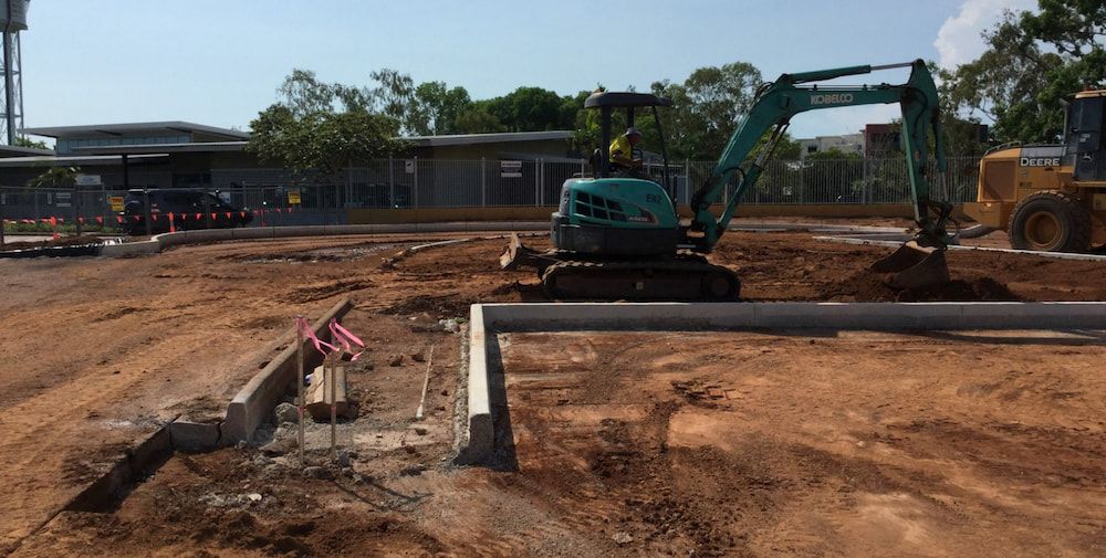 A Man is Driving an Excavator in a Dirt Field — Diggamen Civil Contracting in Tivendale, NT
