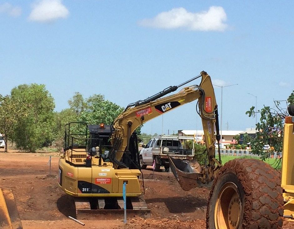 A Cat Excavator is Digging a Hole in a Dirt Field — Diggamen Civil Contracting in Tivendale, NT