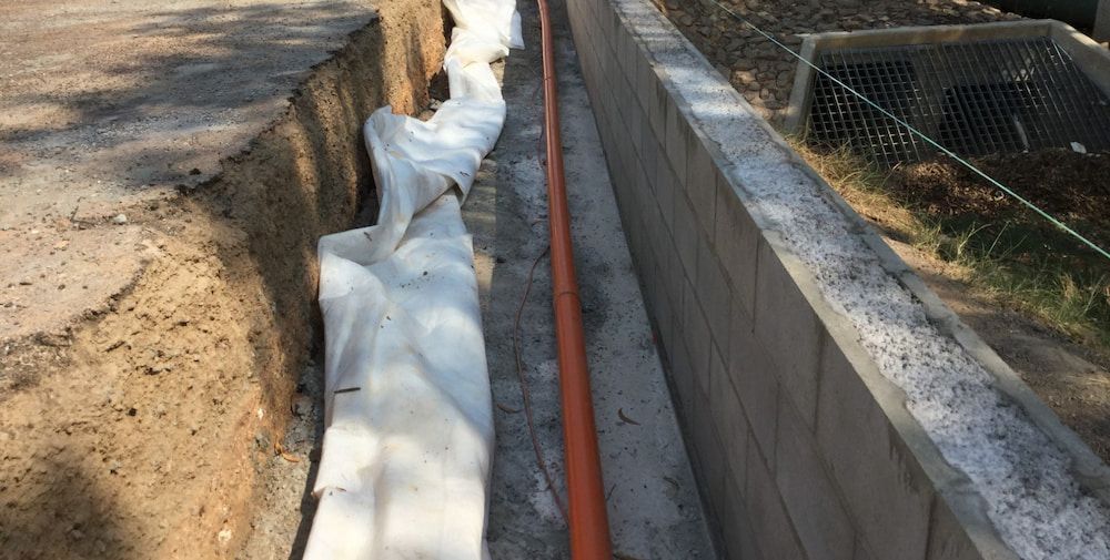 A Pipe is Being Installed in a Trench Next to a Brick Wall — Diggamen Civil Contracting in Tivendale, NT