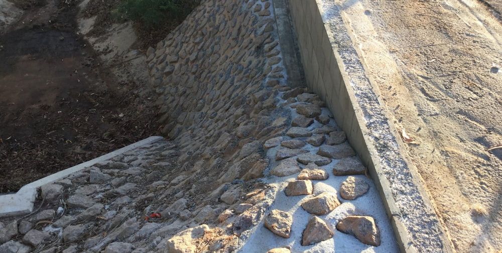 A Stone Wall is Being Built Next to a Dirt Road — Diggamen Civil Contracting in Tivendale, NT