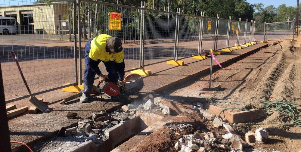 A Man Is Cutting a Hole in The Ground with A Circular Saw — Diggamen Civil Contracting in Tivendale, NT