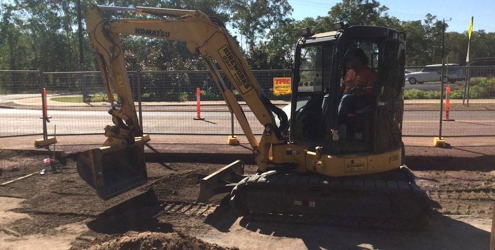 A Man Is Driving a Yellow Excavator on A Construction Site — Diggamen Civil Contracting in Humpty Doo, NT