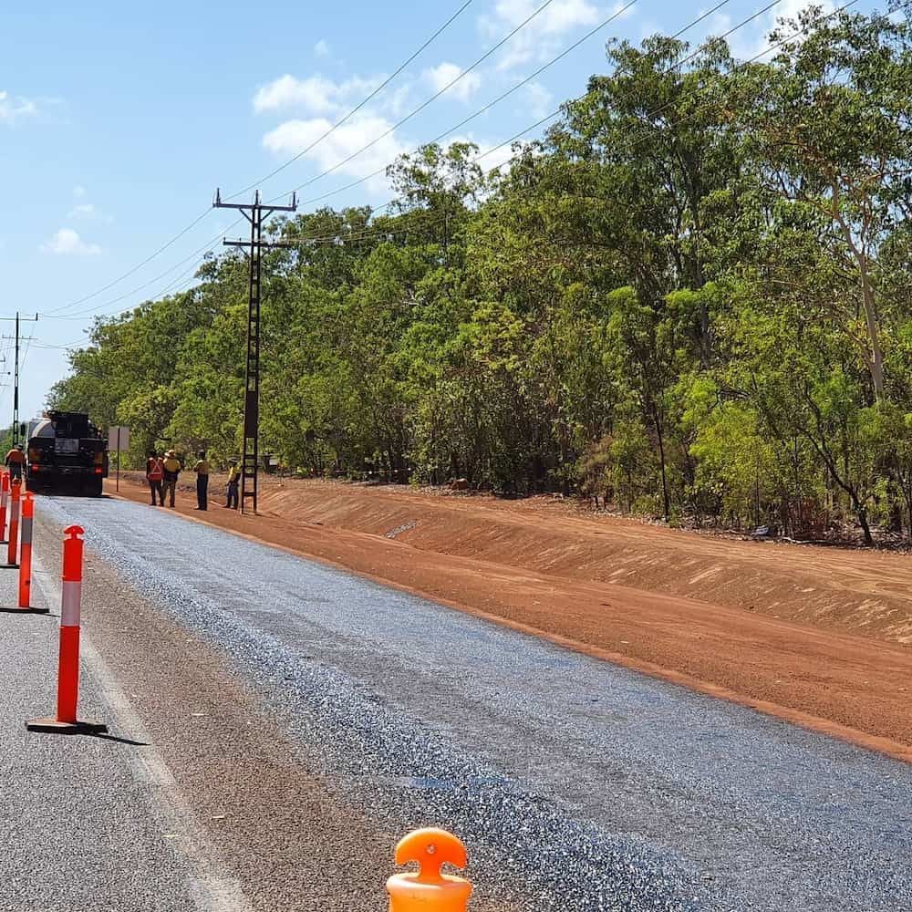 A Truck is Driving Down a Road Next to a Row of Orange and White Poles — Diggamen Civil Contracting in Tivendale, NT