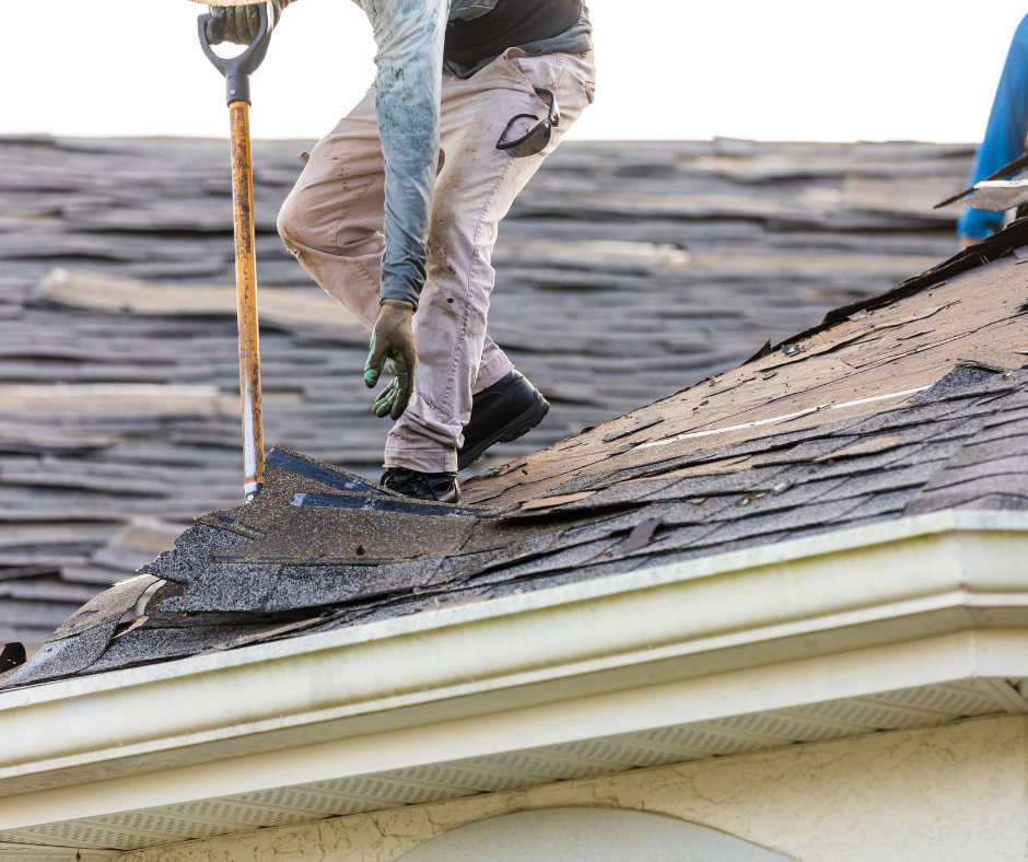 Roofer on a damaged roof removes shingles with a shovel.