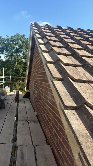 Steep brick roof with wooden shingles beside a scaffold under a blue sky