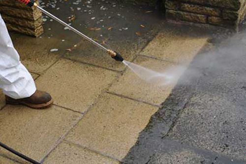 A person is using a high pressure washer to clean a brick walkway.