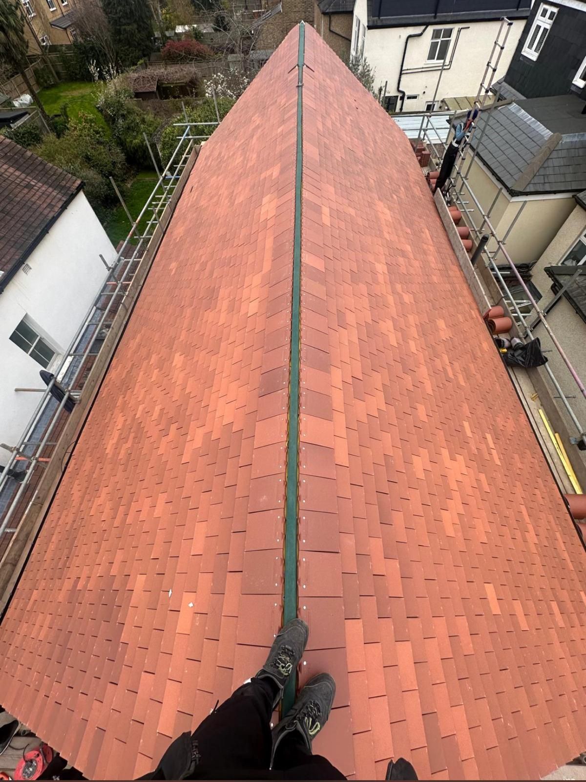 Person's feet on terracotta tile roof, centered down the ridge. Scaffolding on both sides.