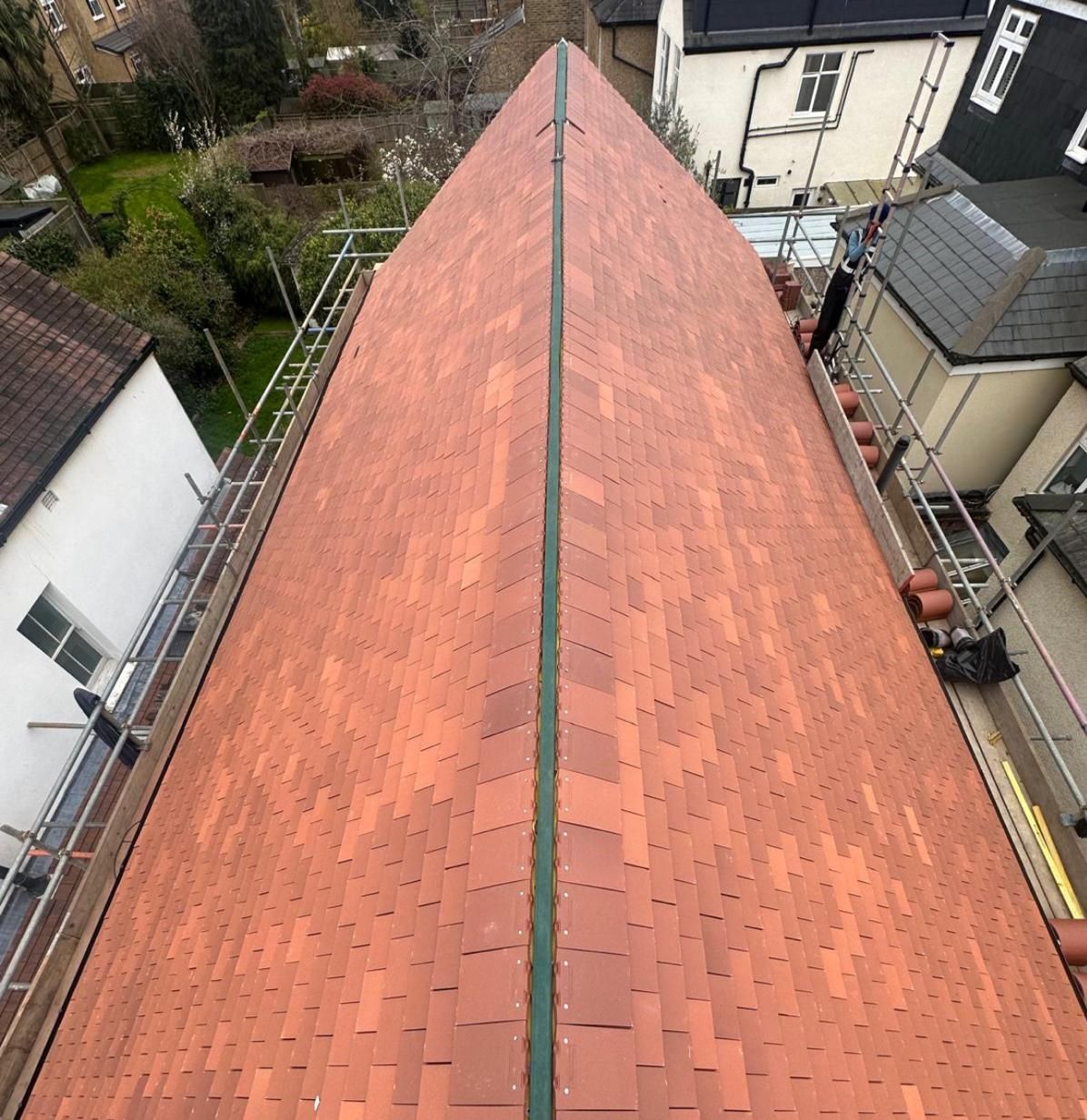 View of a red tiled roof by fixall roofing, with a central seam, from above; scaffolding on sides.