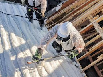 A man is spraying foam on the roof of a building.
