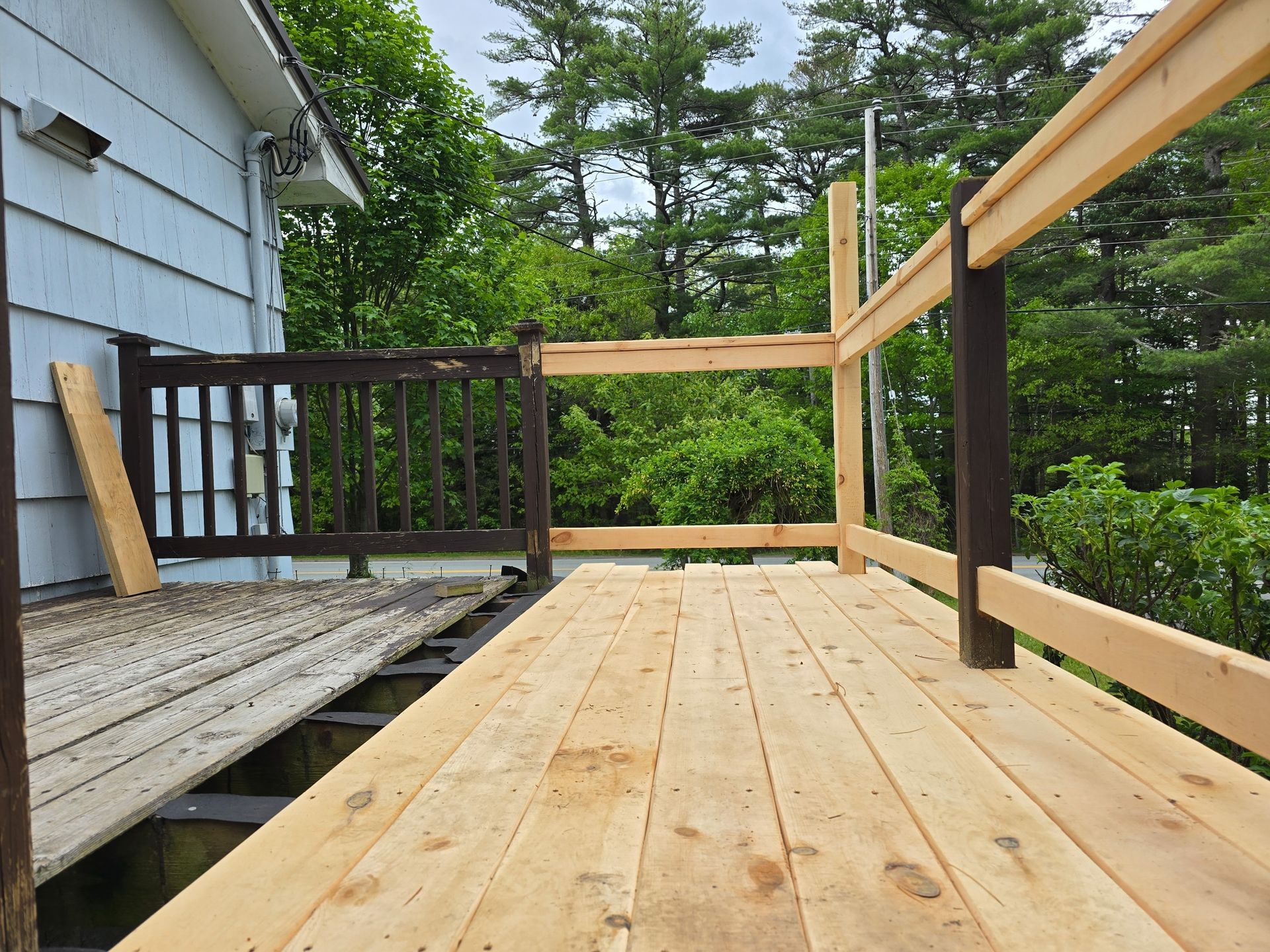 Wooden deck construction; new deck boards laid; railing posts and rails partially built.