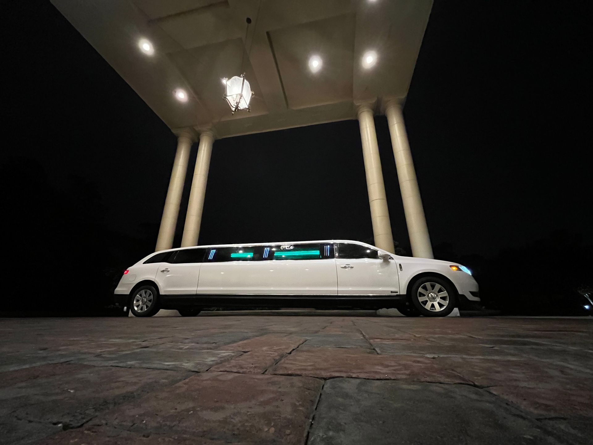 White limousine parked under a lit overhang at night, illuminated from above.