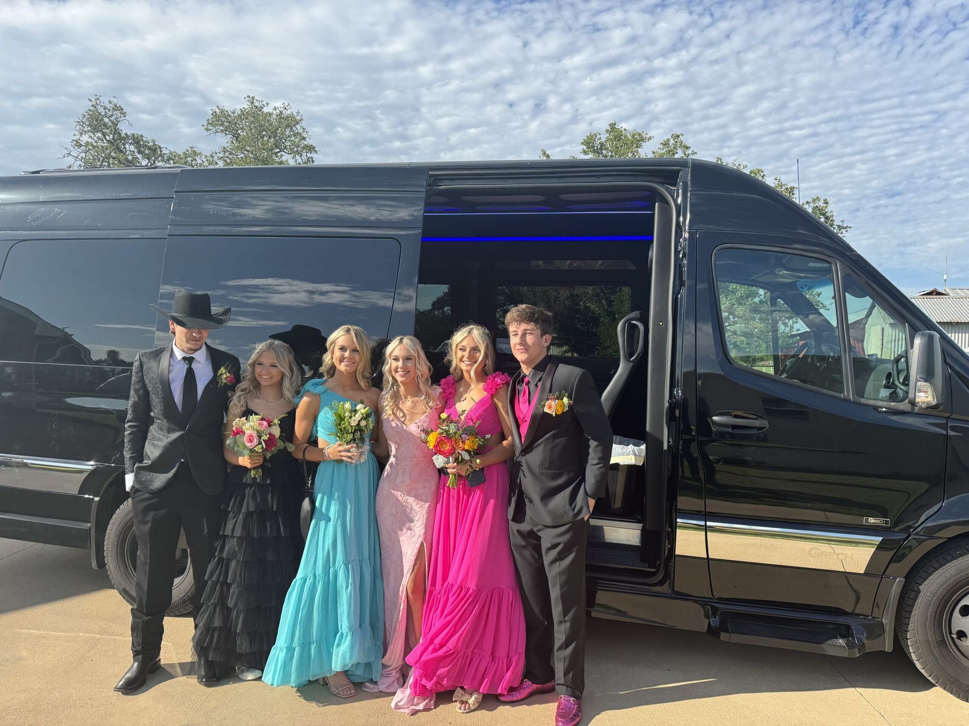 A group of people in prom dresses are standing in front of a black van.