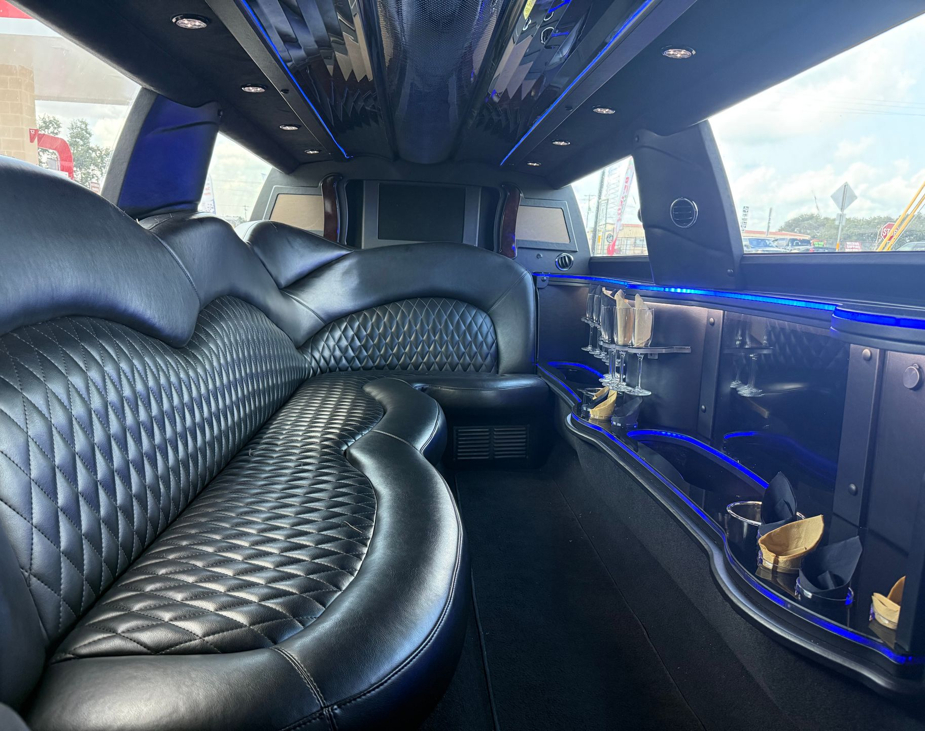 Interior of a black limousine with black quilted leather seating, neon blue lights, and a bar area.