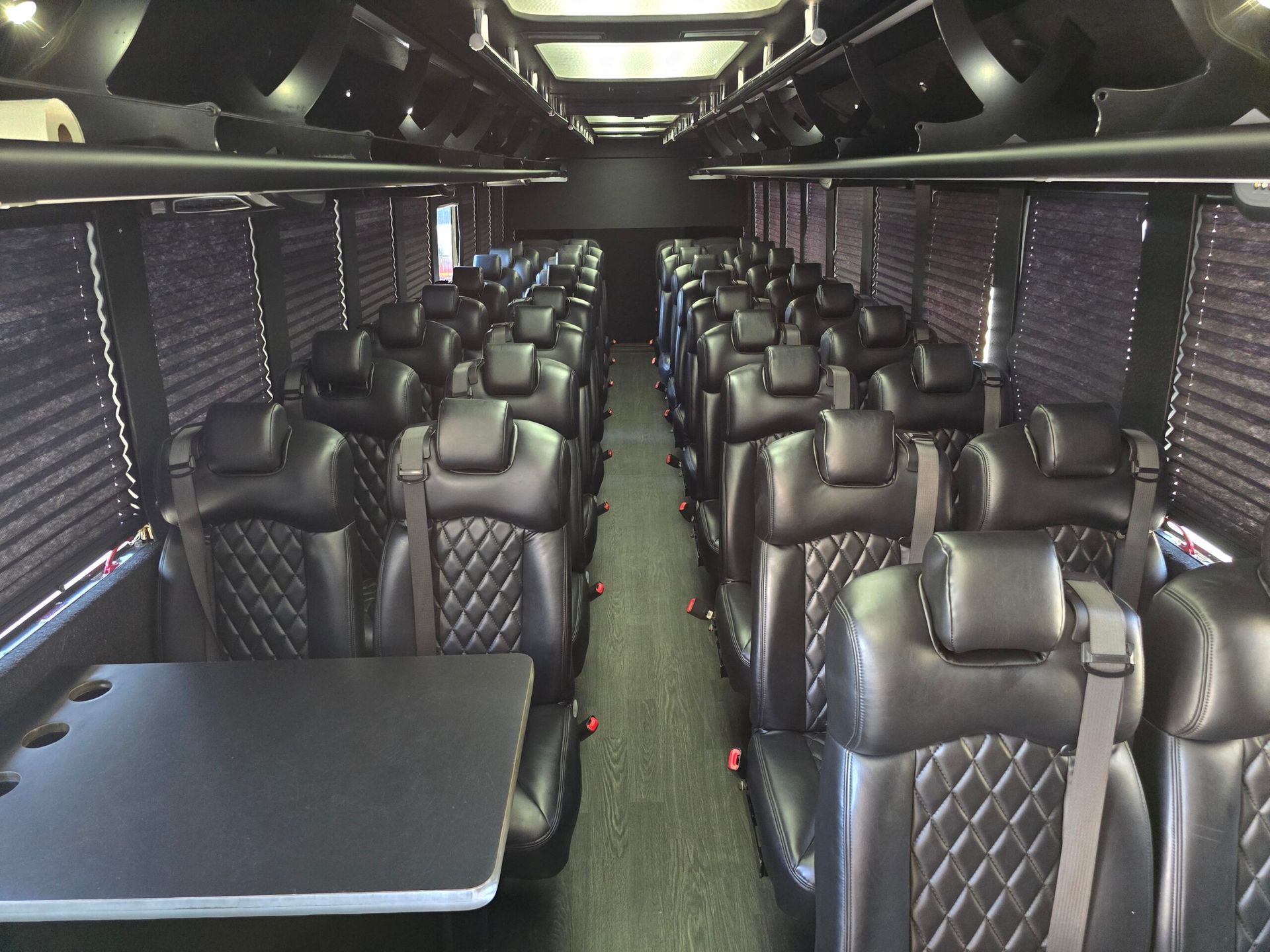 Interior of a black luxury bus with diamond-stitched leather seats, tables, and window blinds.