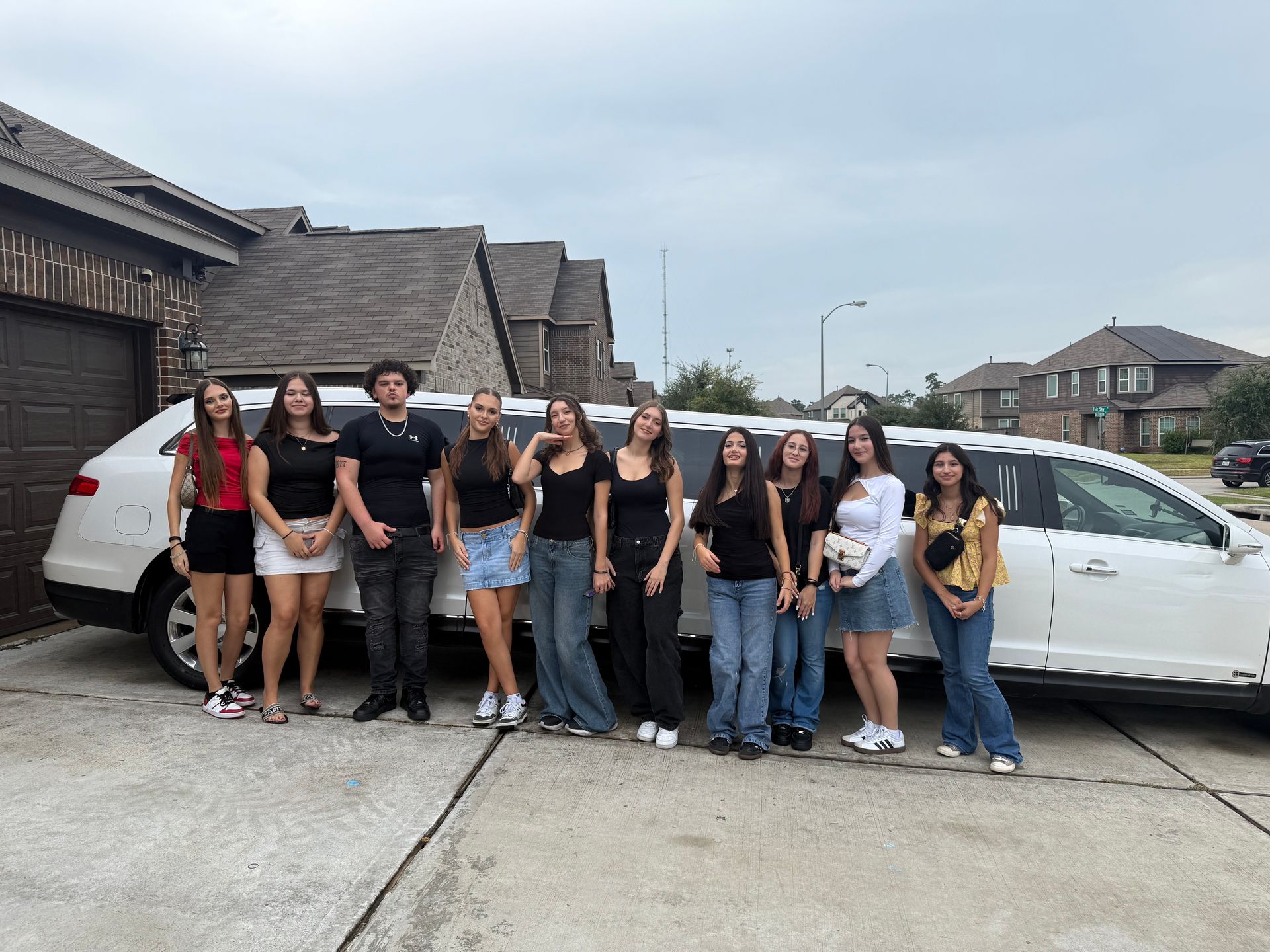 A group of people poses next to a white limousine in a driveway.