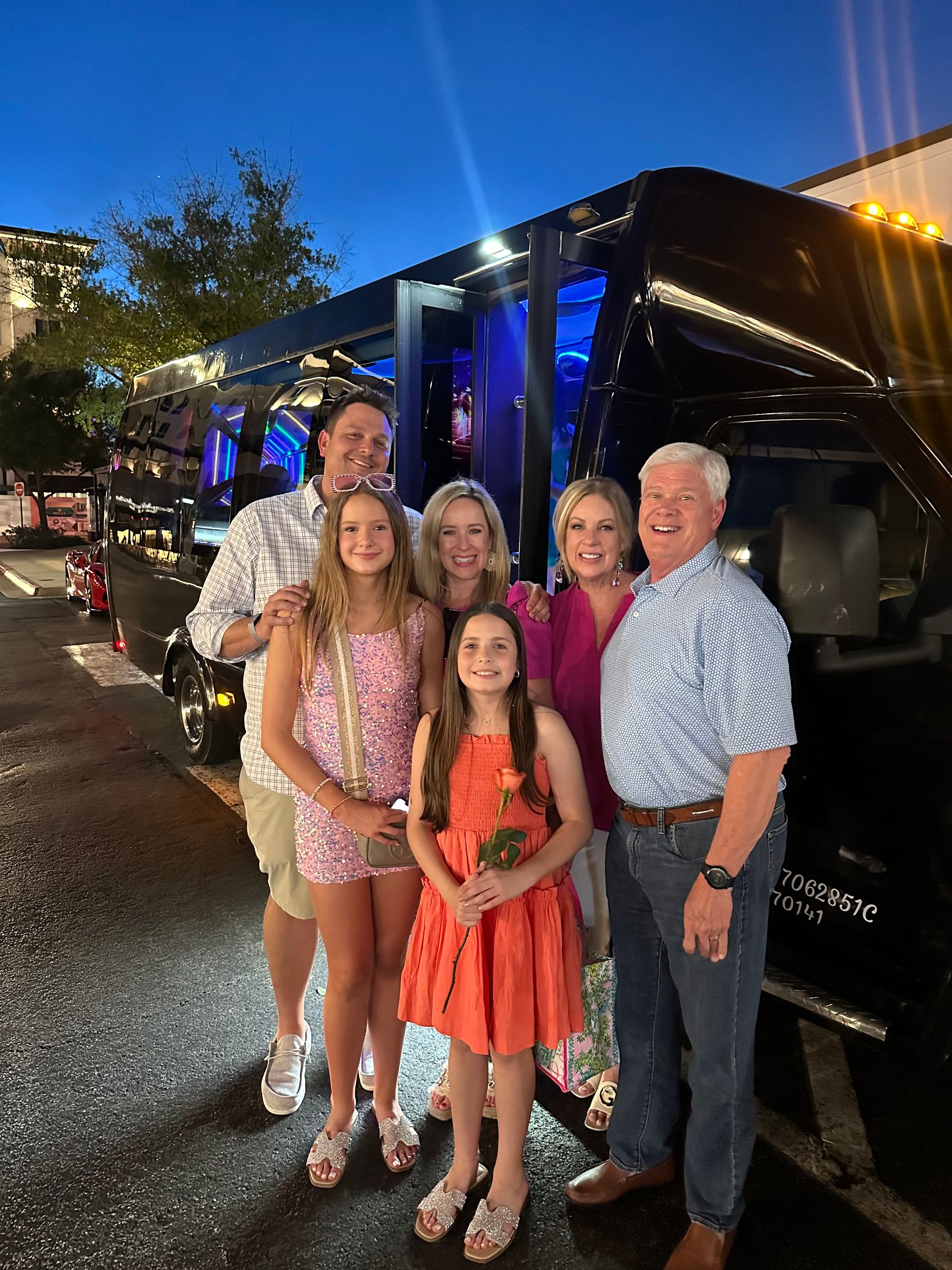 A group of seven people pose in front of a black vehicle at night.