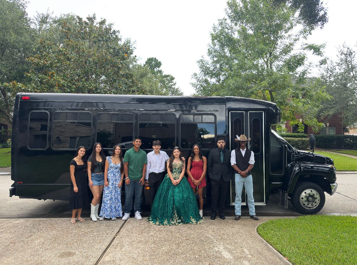 Group of people posing by a black party bus; some are wearing formal attire, standing on a driveway.