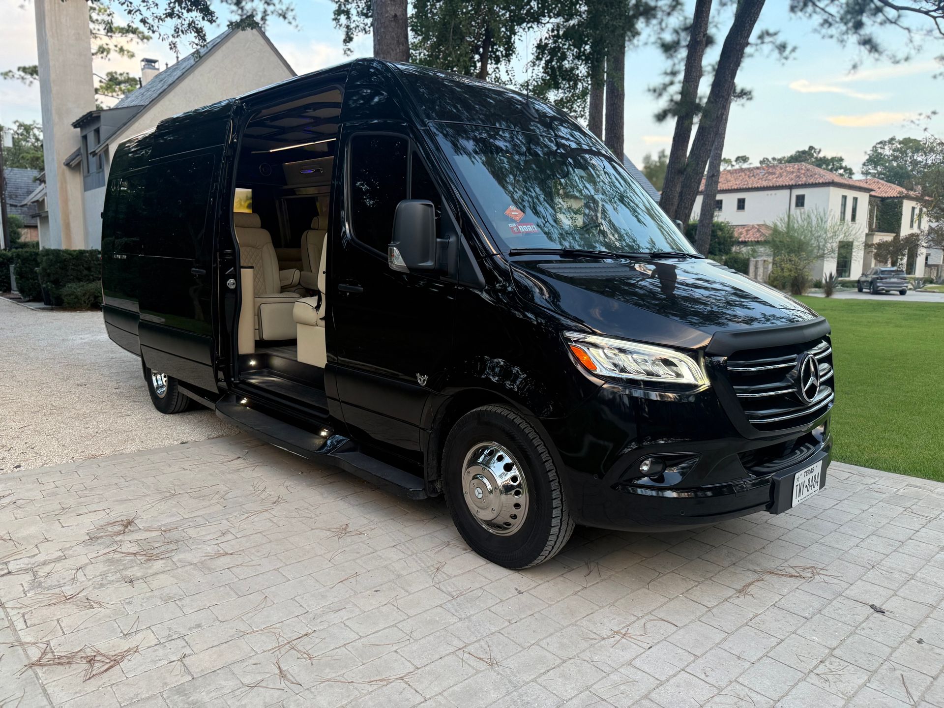 Black Mercedes-Benz Sprinter van parked on a stone driveway, door open, in front of a house.