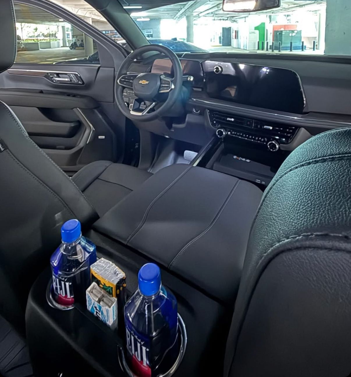 Interior of a dark-colored car. Center console with water bottles. Dashboard and steering wheel visible.