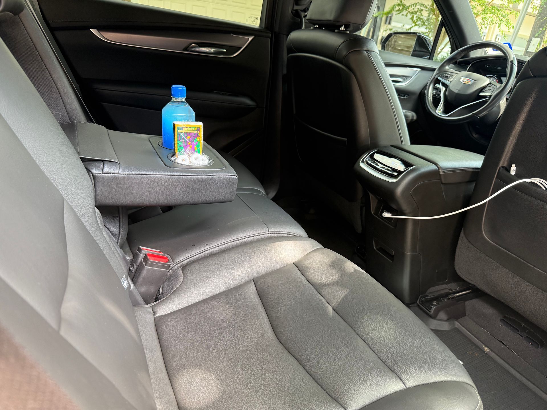 Backseat of a black Cadillac SUV with a fold-down armrest holding a blue water bottle and other items.