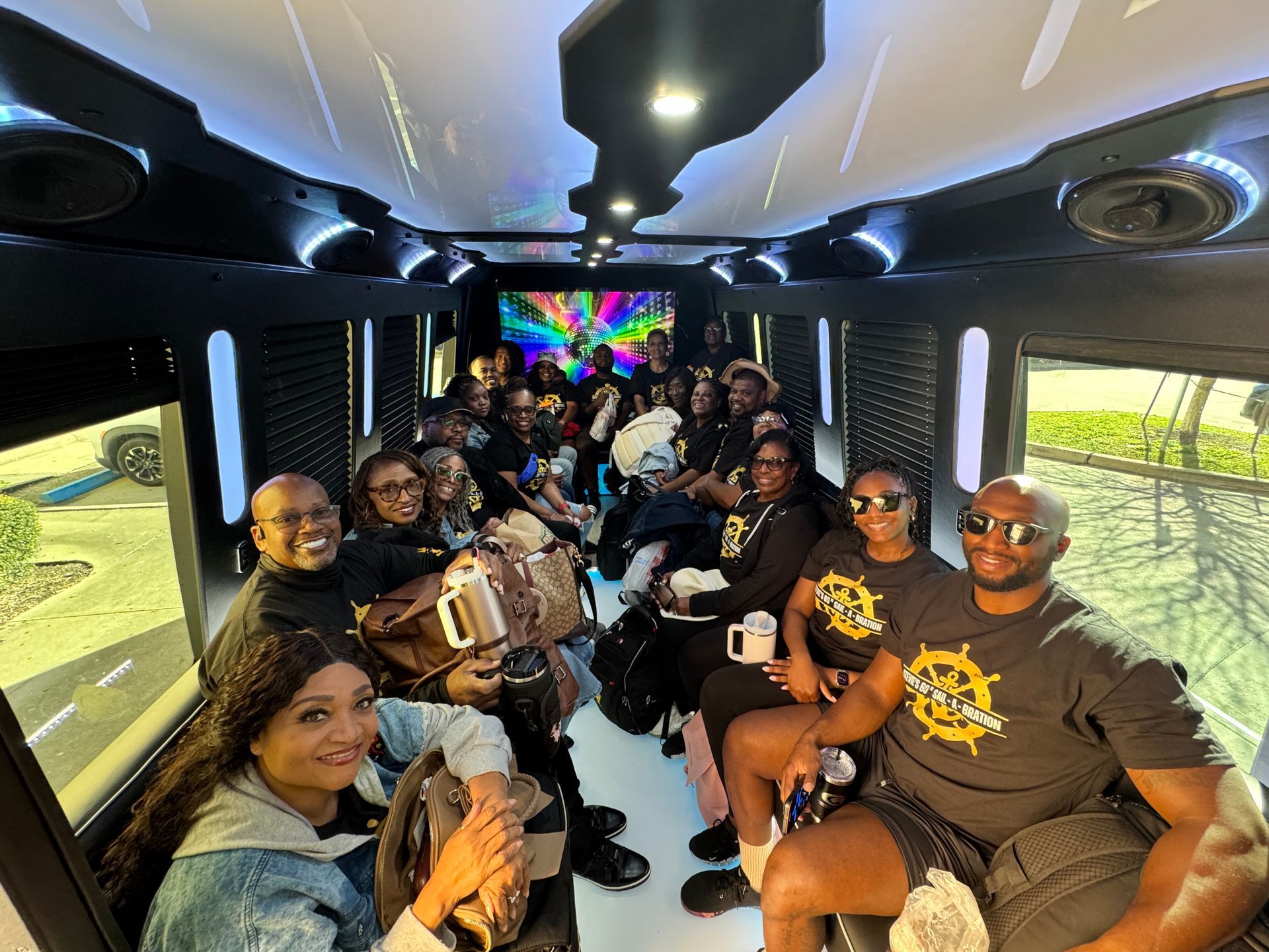 People seated inside a party bus, some smiling. Colorful lights above.