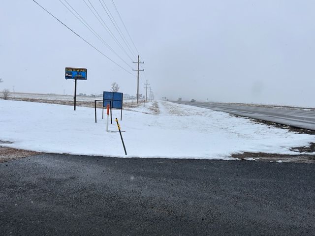 Snow-covered rural roadside with utility poles and signs under a gray sky