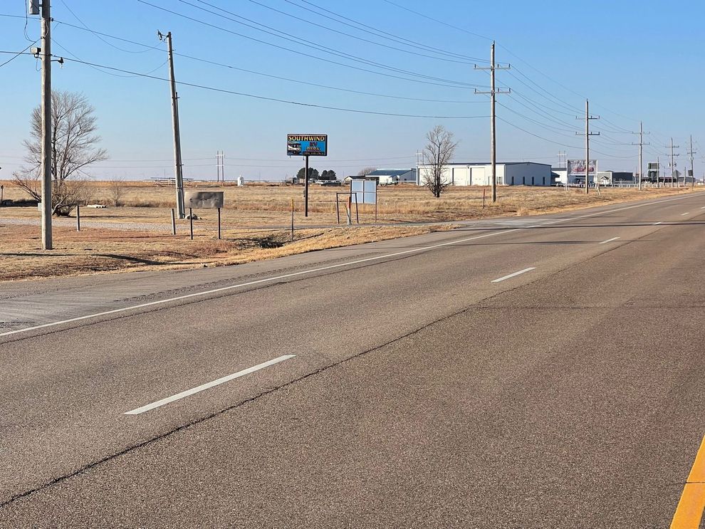 Empty rural road beside dry fields under a clear blue sky