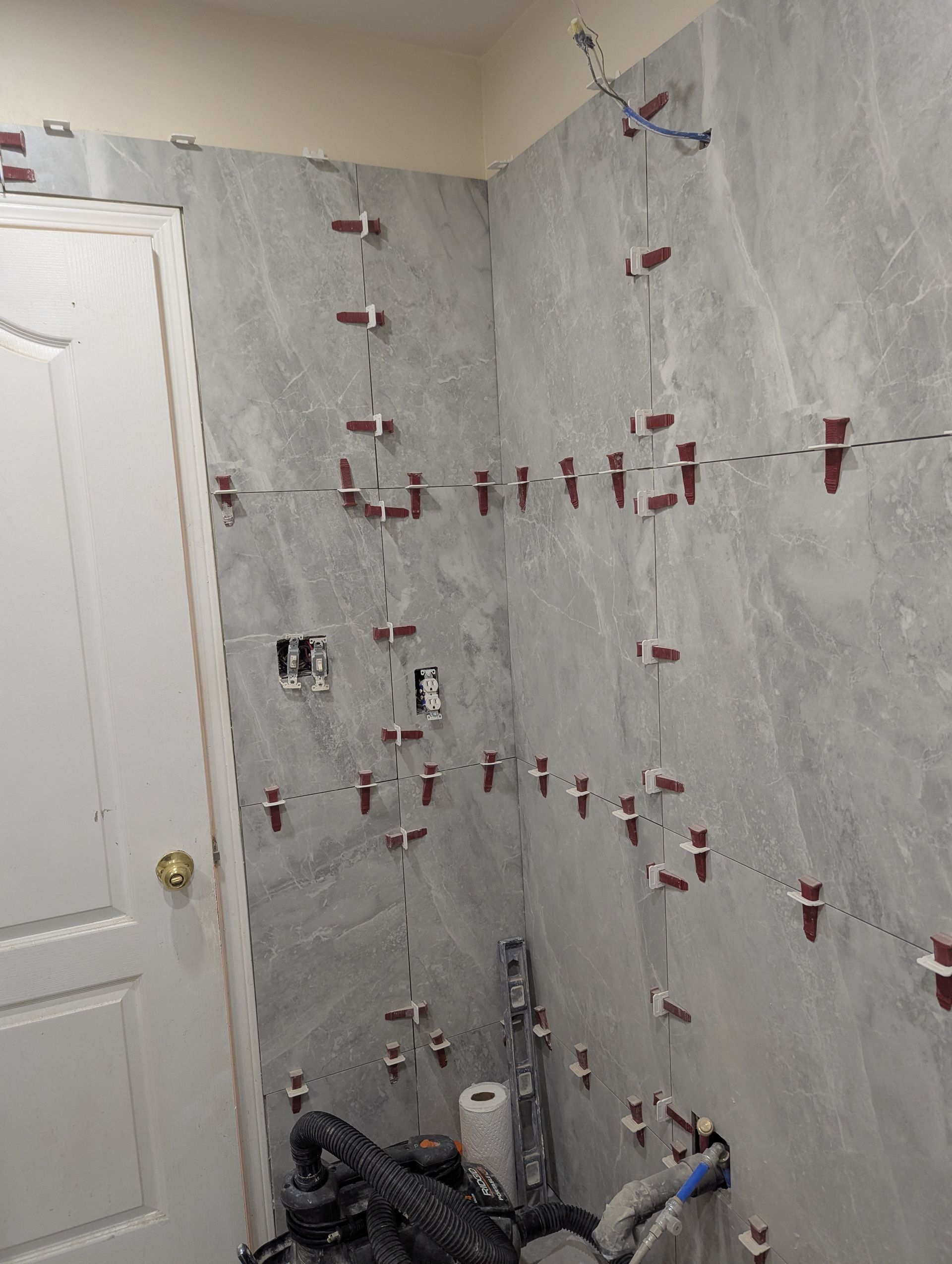 Partially tiled bathroom wall with red spacers and plumbing fixtures under installation
