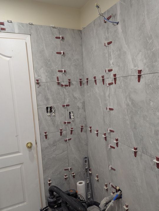 Bathroom wall with gray tile, red spacers, and plumbing fixtures under renovation