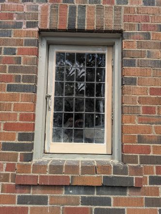 Small white-paned window set in a brick wall with dark reflective glass.