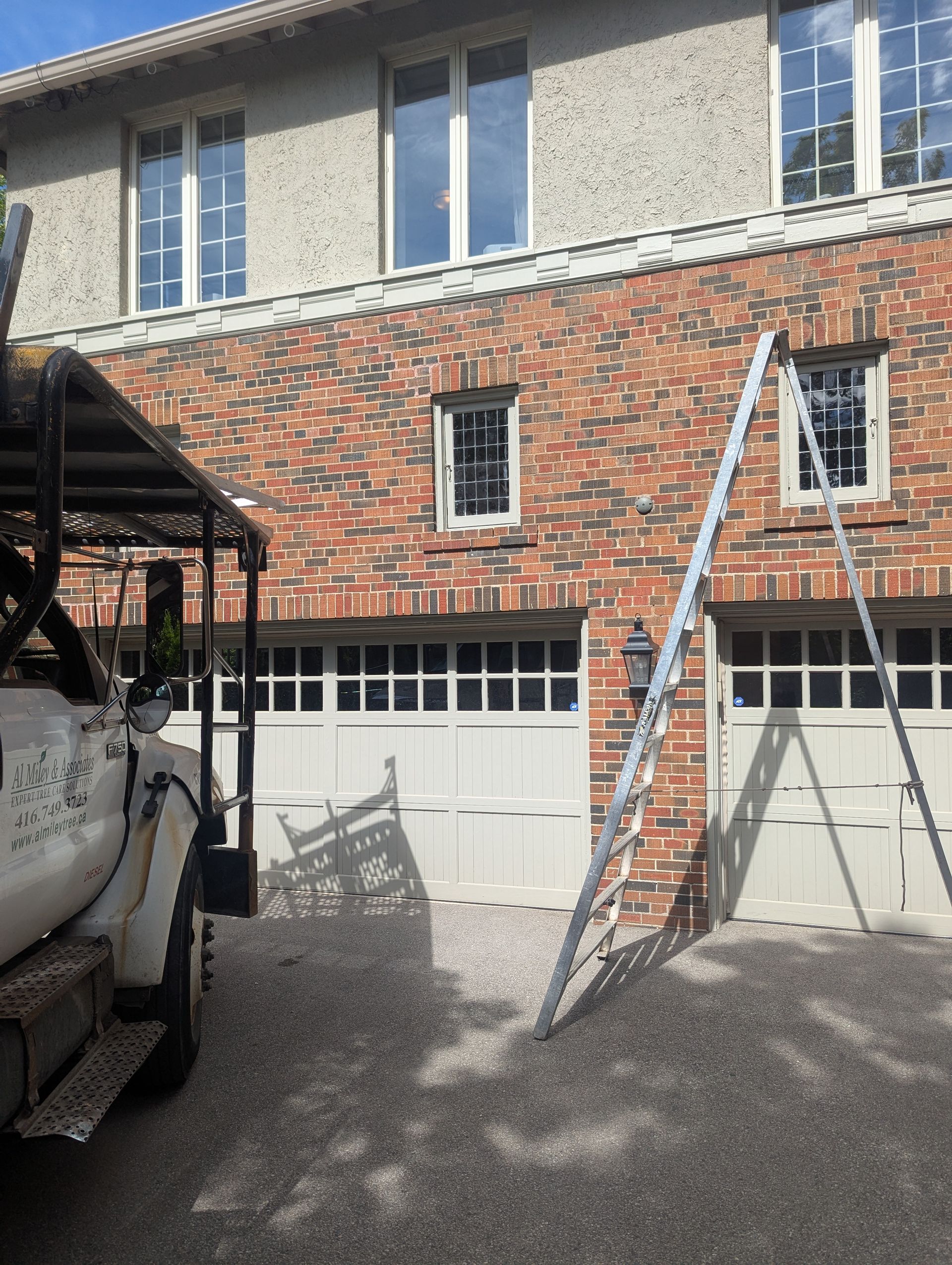 Brick townhouse exterior with two garage doors and a ladder leaning against the wall