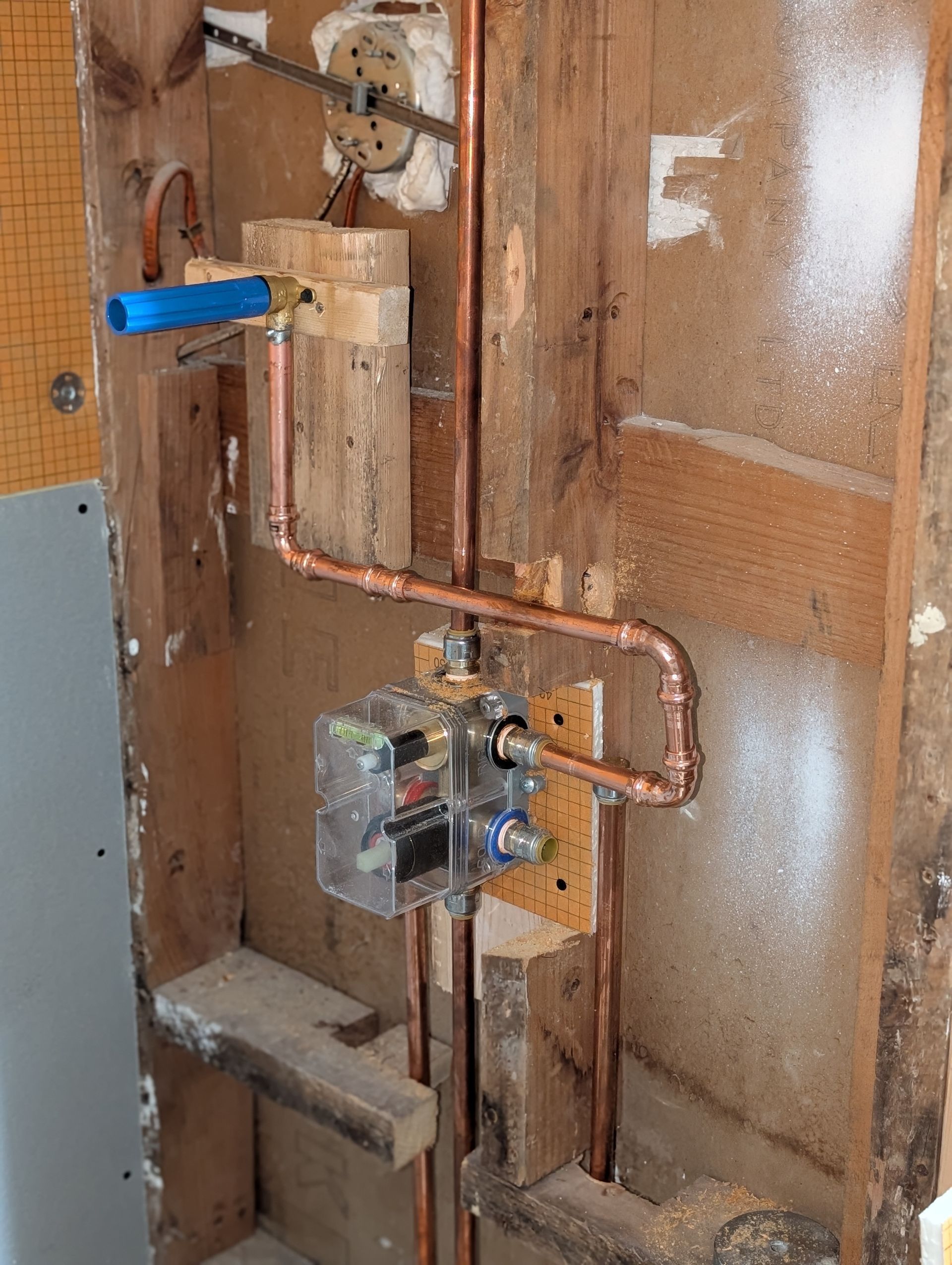 Exposed copper plumbing and a blue shutoff valve inside an unfinished wall cavity