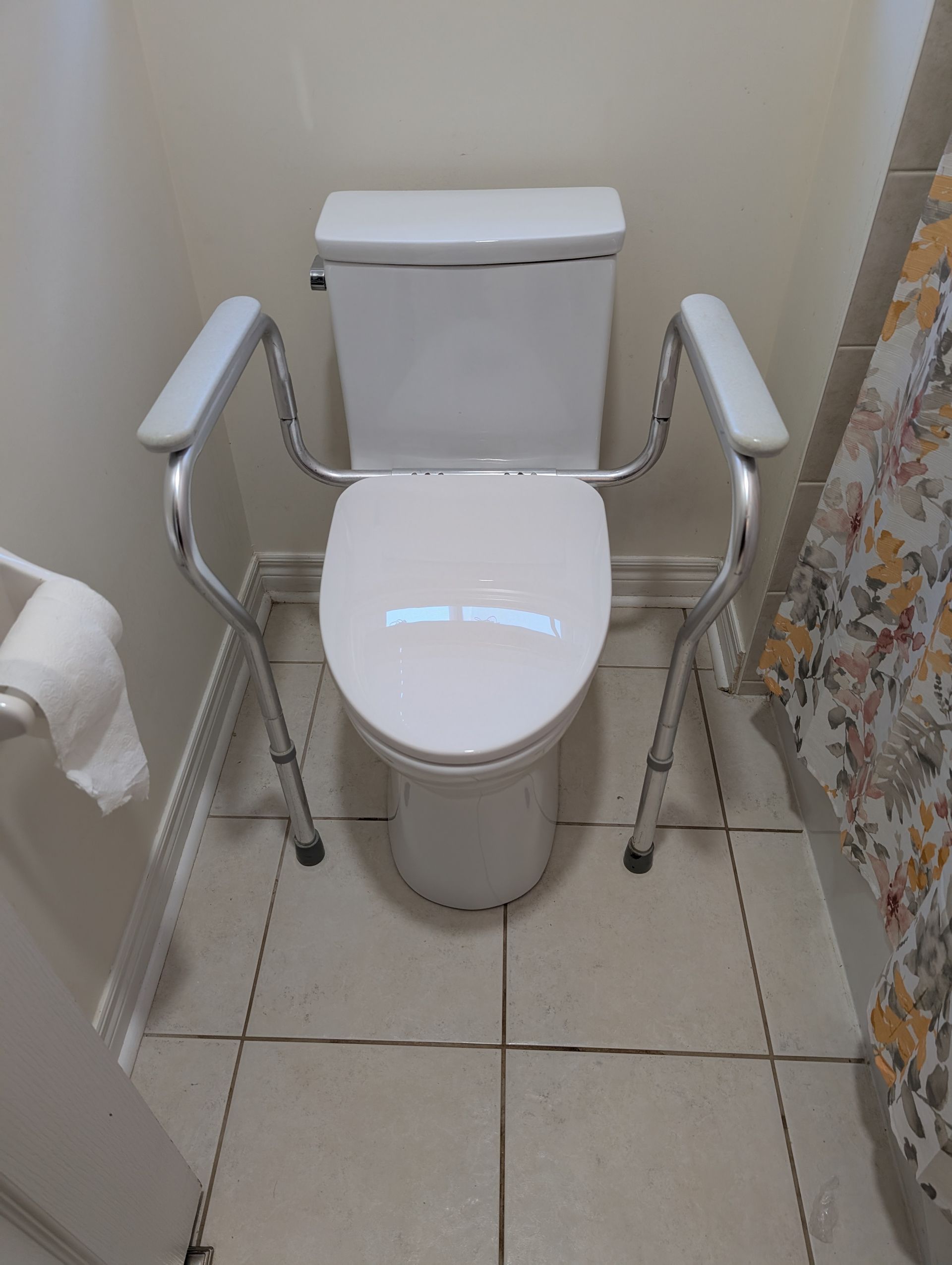 White toilet with metal safety rails in a small tiled bathroom.