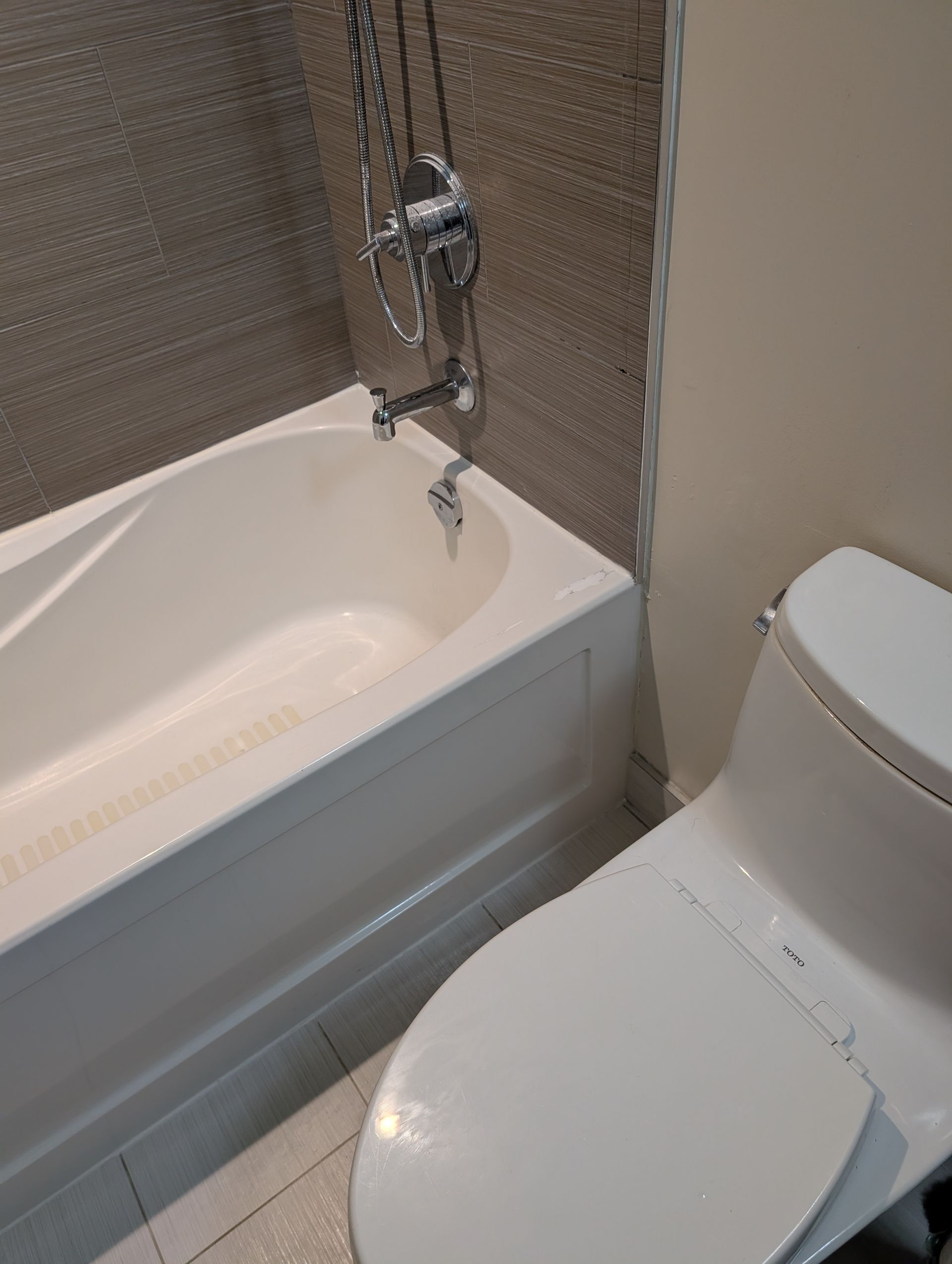 Small bathroom with a white toilet beside a bathtub and shower tile wall.