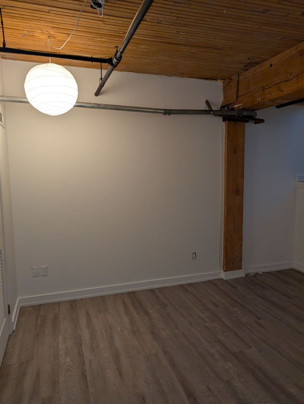 Empty room with white walls, wood ceiling, exposed beam, and gray flooring.