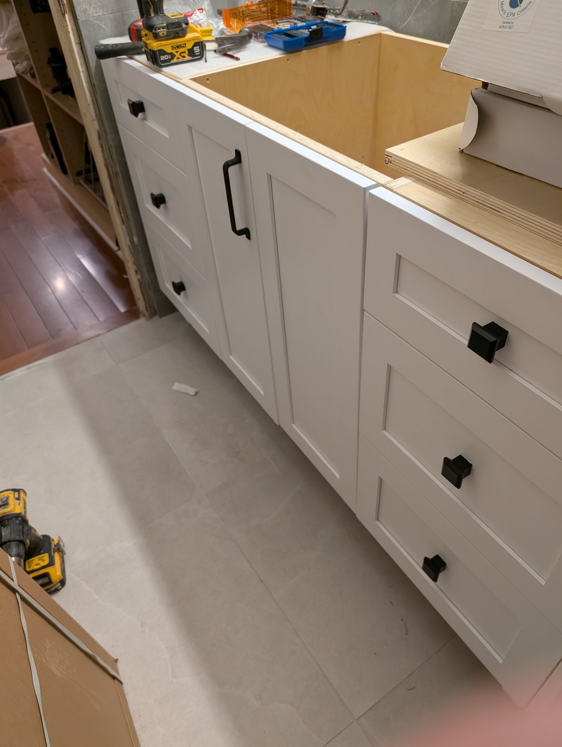 Partially renovated kitchen with white cabinets, missing countertop section, and tools on the floor
