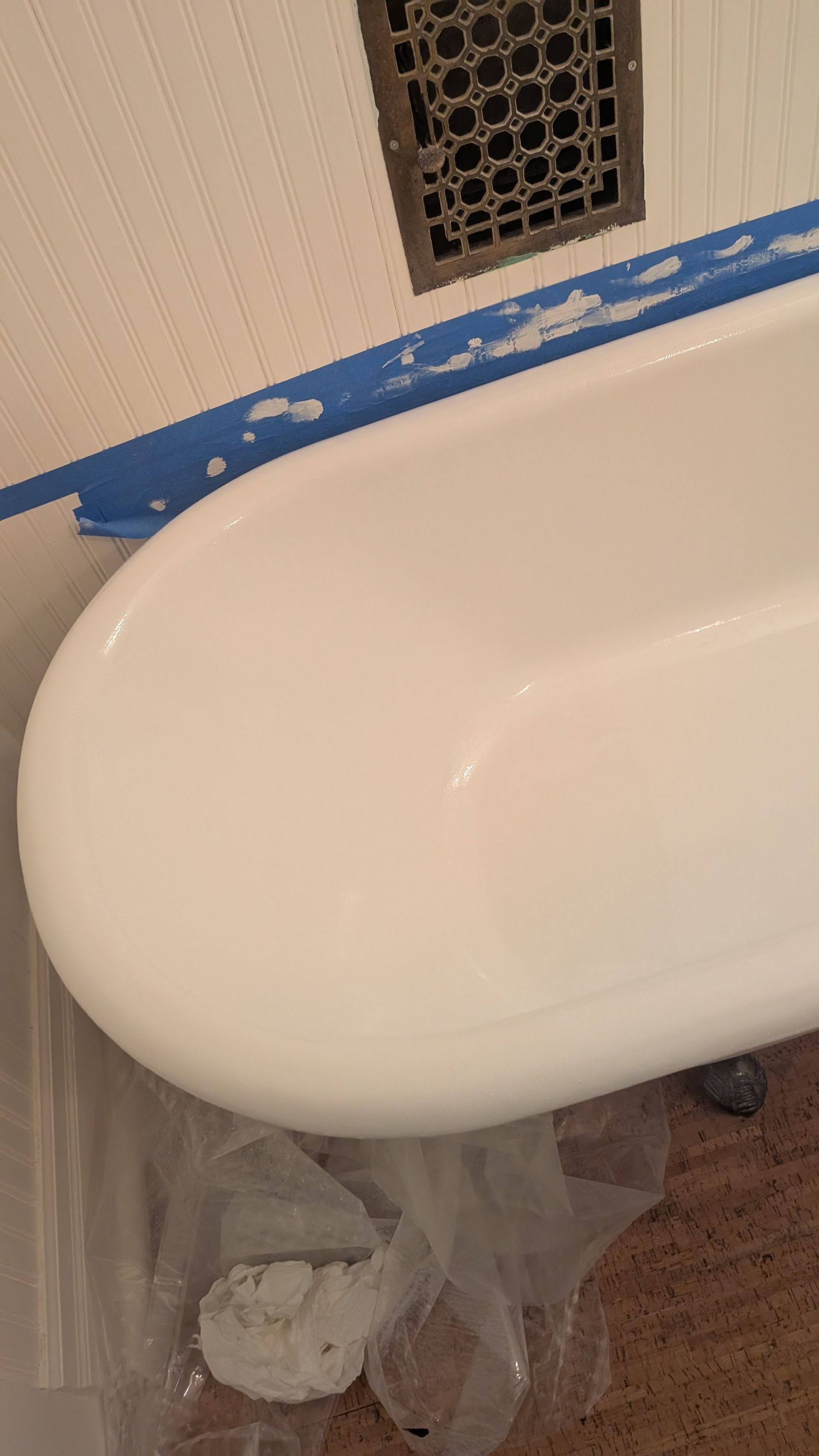 Close-up of a white bathtub edge taped off in a bathroom under renovation, with plastic sheeting below.