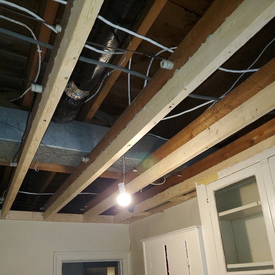 Basement with exposed ceiling beams, ductwork, and a hanging light above white walls and a door.
