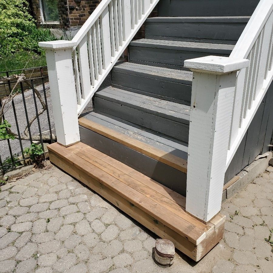 Wooden ramp at the base of a white porch staircase on a stone patio.