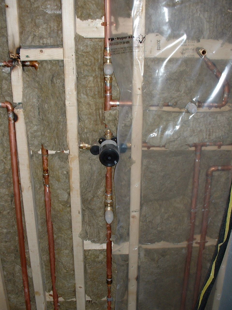 Insulated wall with exposed copper pipes and a black valve in a construction or utility space