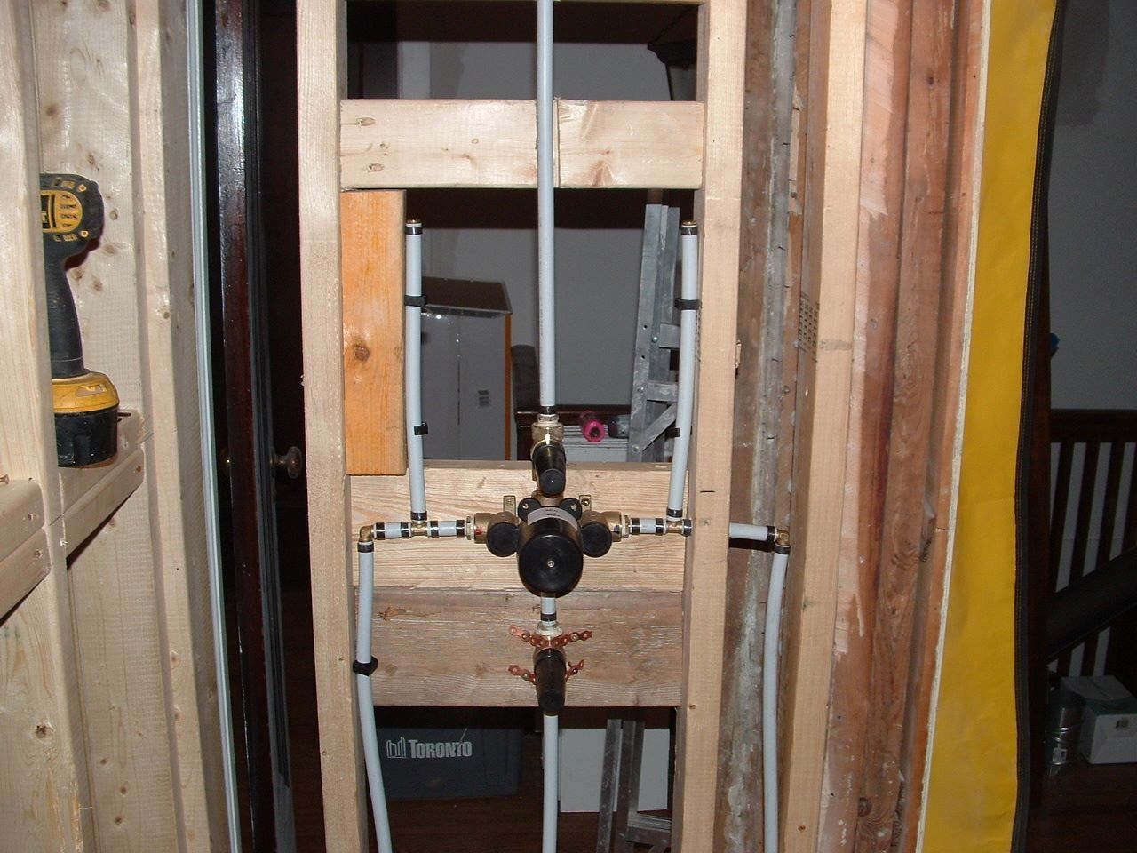 Pipe manifold with valves mounted between wooden studs in an unfinished wall.