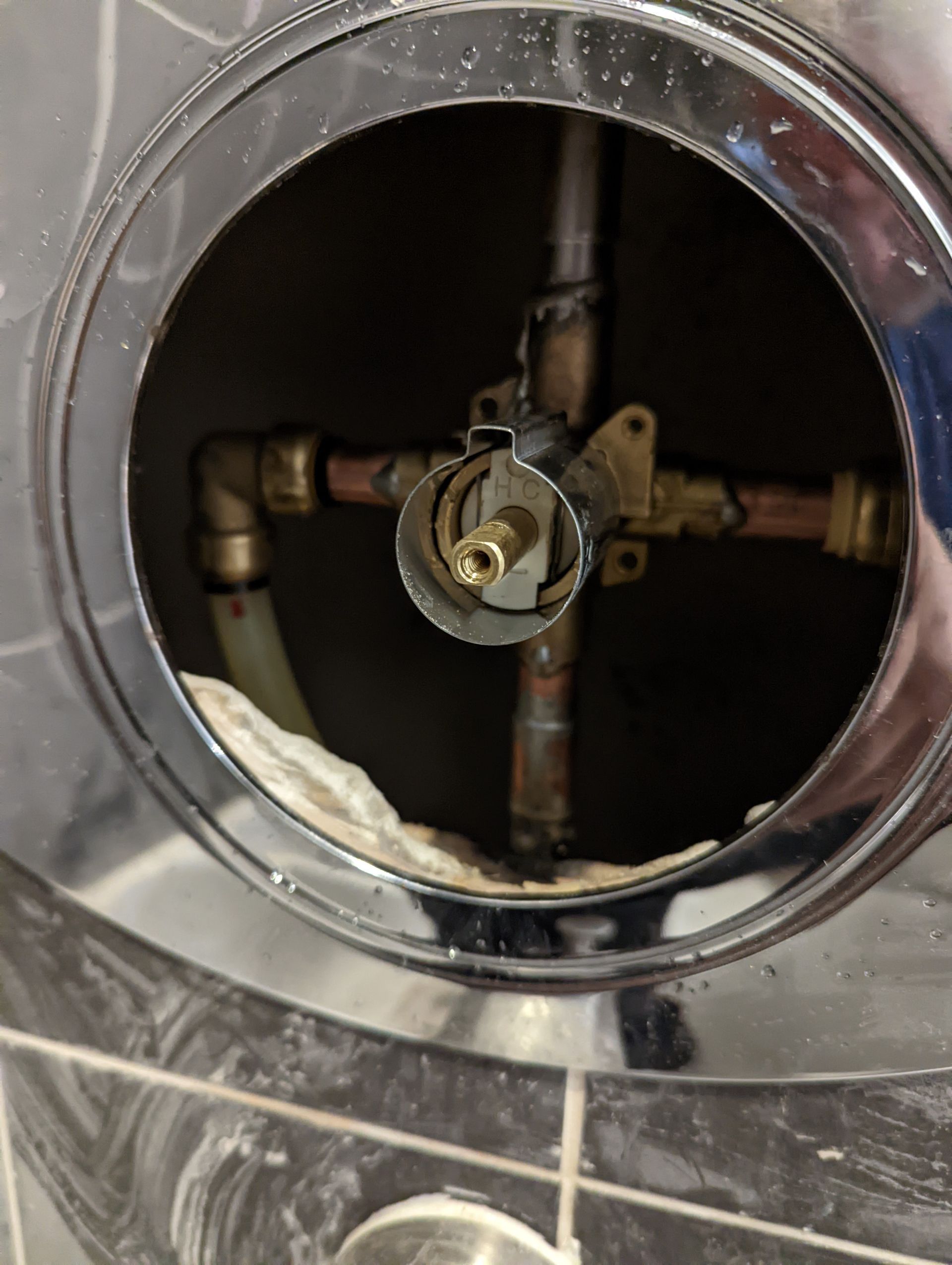 Circular wall opening showing exposed plumbing pipes and a central brass valve in a chrome fixture.
