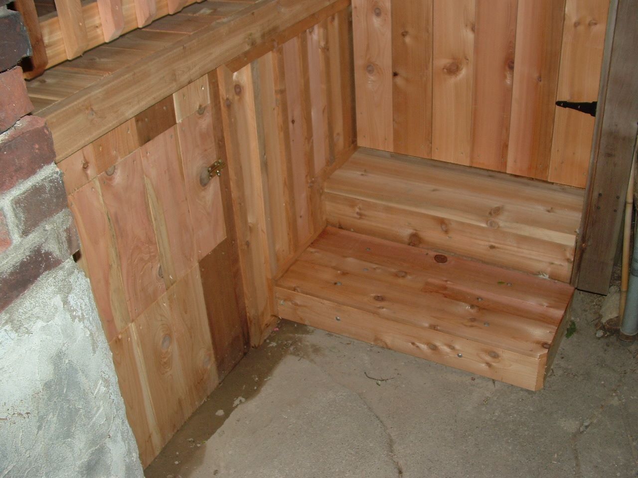 Wooden bench seating built into a paneled corner beside a brick wall on a concrete floor
