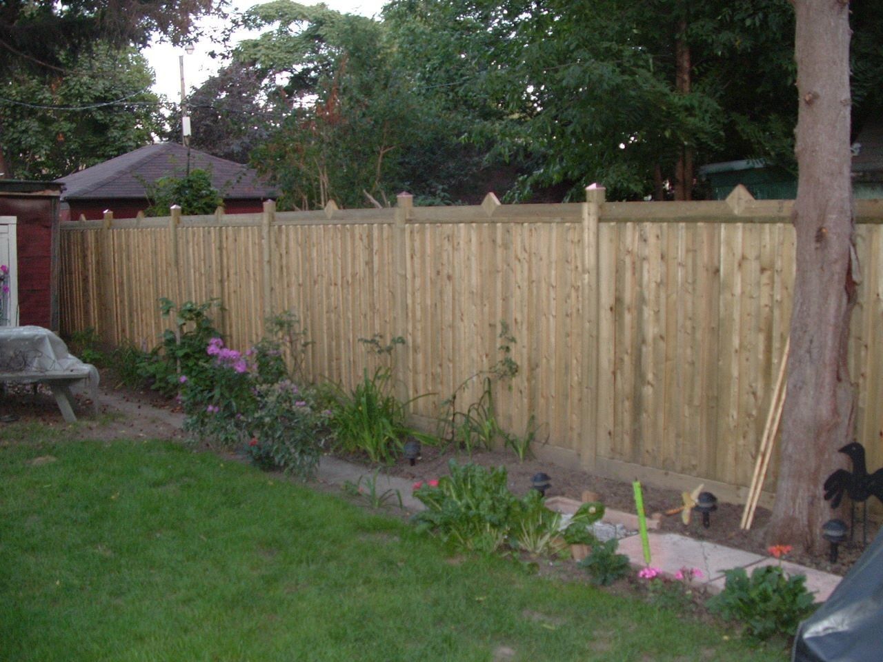Backyard with a new wooden privacy fence, small garden bed, and green lawn.