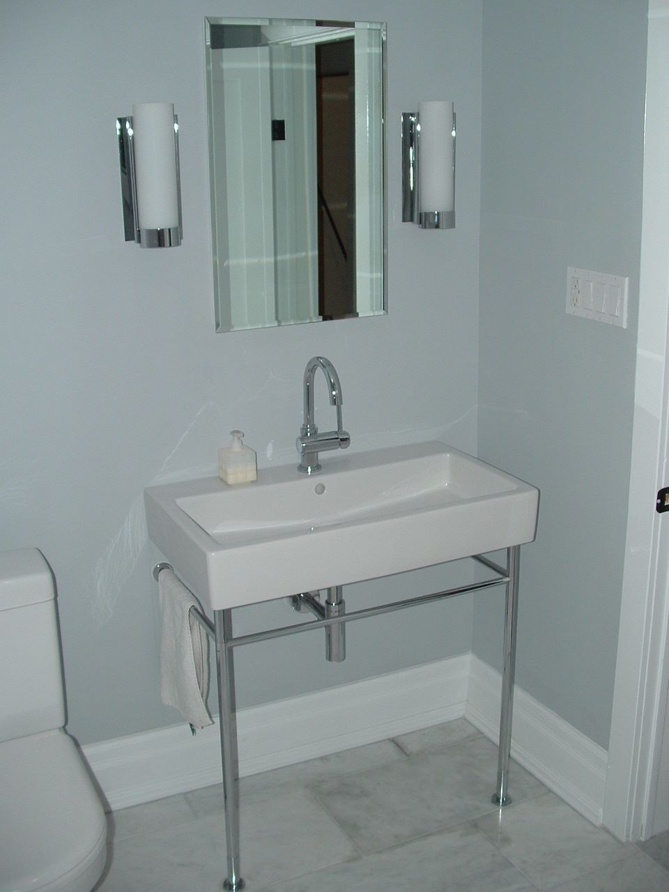 Accessible bathroom sink with mirror, grab bars, and toilet partially visible