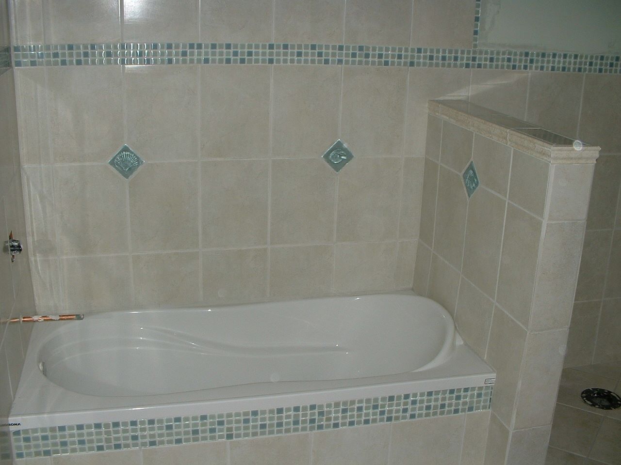 Bathroom with a beige tiled bathtub and decorative blue tile accents.