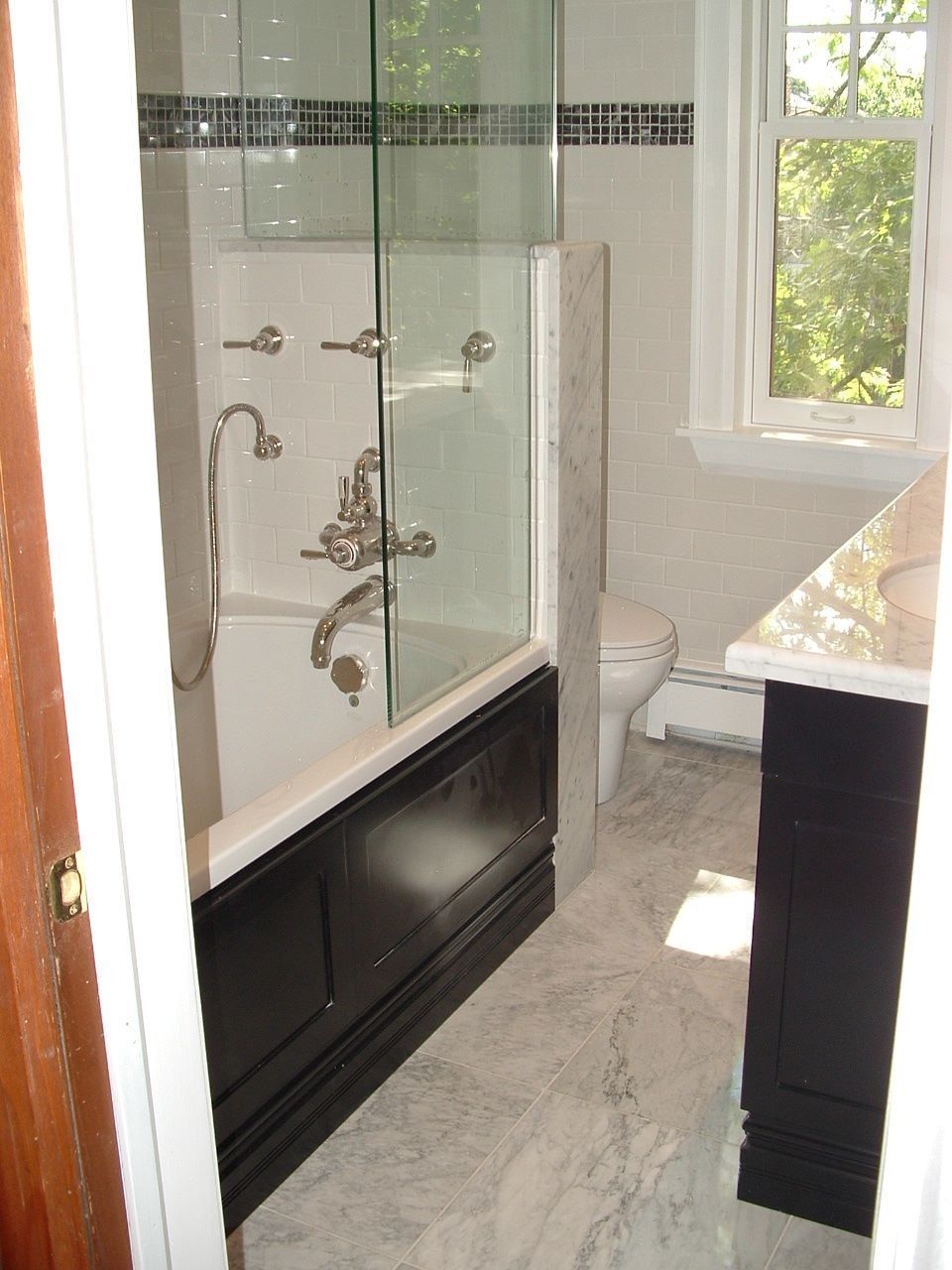 Small bathroom with glass shower enclosure, dark vanity, and window letting in daylight.